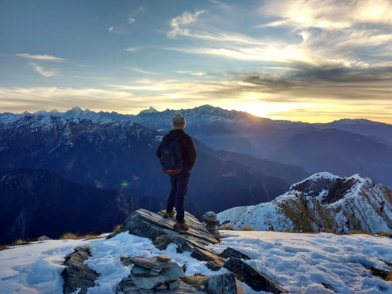 man hiking in snowy mountains at sunset home alone for the holidays
